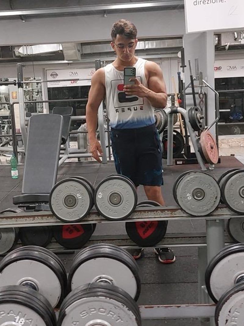 Damiano Tropea in palestra, davanti allo specchio tra i manubri, in canotta bianca
