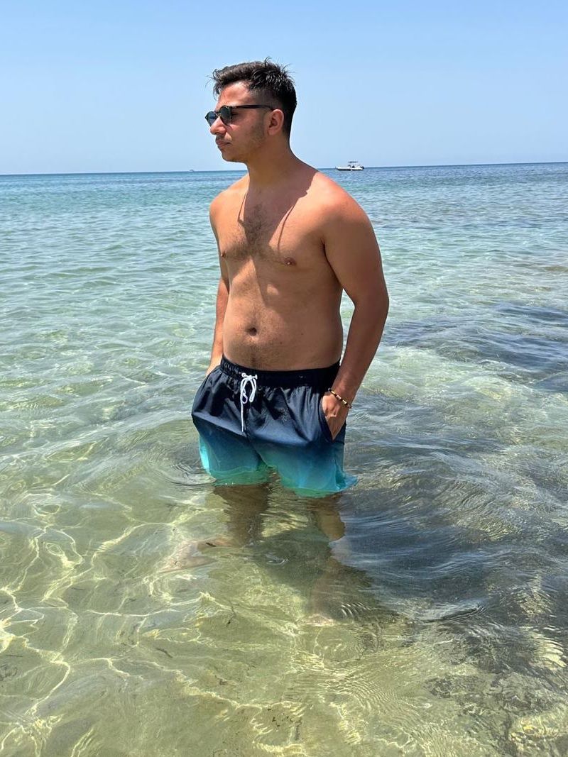 Damiano Tropea in piedi nell'acqua del mare con gli occhiali da sole